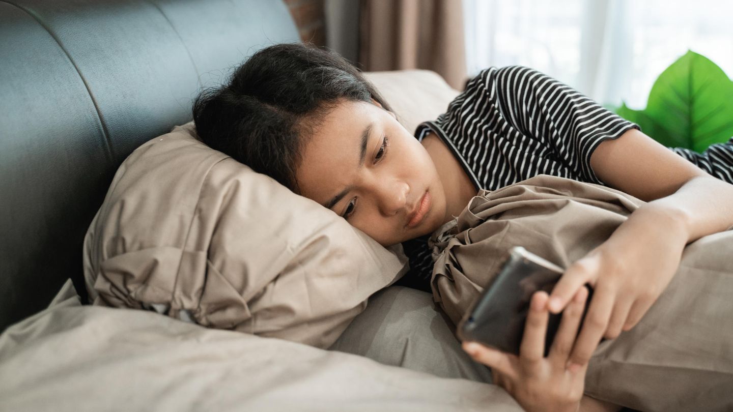 Ein trauriges Mädchen liegt mit ihrem Handy im Bett