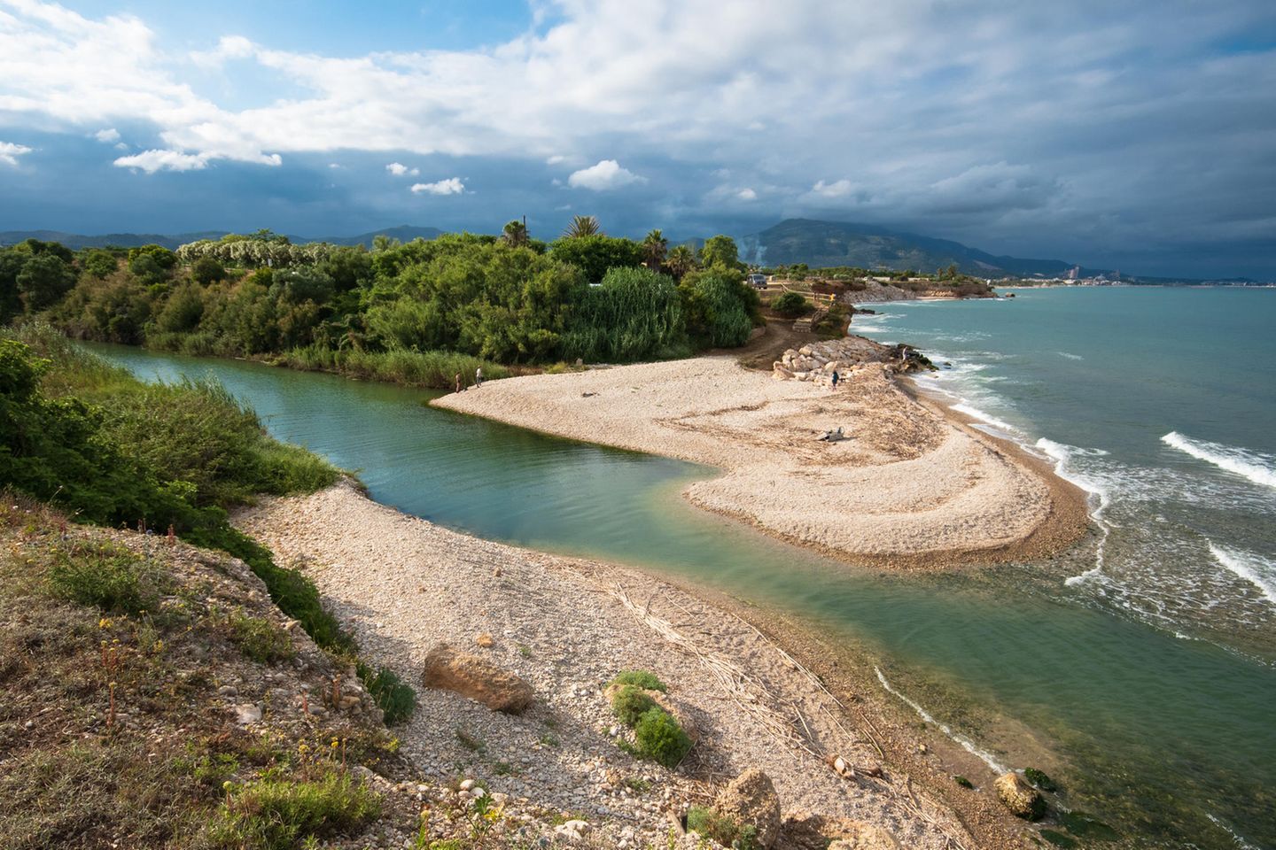 An diesem herrlichen Kieselstrand an der Mündung des Riu Sénia haben Sie die Wahl zwischen einem Bad in Salz- oder Süßwasser. Je nach Wetterverhältnissen kann man manchmal zum gegenüberliegenden Ufer waten. Der Fluss bildet die Grenze zwischen Valencia und Katalonien. Durch die hohen Klippen wirkt die Bucht von oben unerreichbar, doch es gibt einen Weg um die Landspitze. Wildblumen, darunter auch „herzblättrige Mittagsblumen“, säumen den Strand, und Zugvögel nisten im Delta stromaufwärts. Schön zum Angeln und fürs Familienpicknick.   Wegbeschreibung: Von Vinaròs auf der N-340 für 6 km Richtung Nordosten, rechts auf die Par- tida el Camaril und nach 400 m oberhalb vom Strand rechts parken. Oder von der Cala de Sòl de Riu zu Fuß 1,25 km über den Küstenweg. Am Fluss links, dem Weg folgen bis zum Schild Riu Sénia (rechts) und über die Stufen zum Strand. Um die Landspitze herum zum Hauptstrand der Platja del Riu de la Sénia.   Erreichbarkeit: Leicht 3 Min.