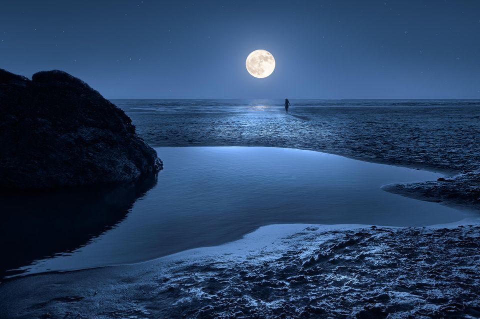 Eine Frau läuft bei Mondschein zum Meer