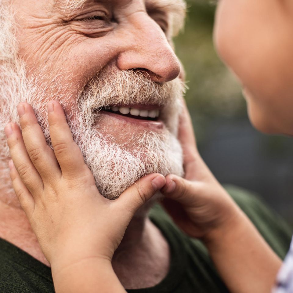 Ein Großvater lächelt seine kleine Enkelin auf seinem Arm an