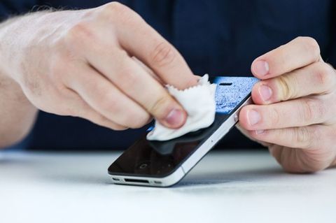 Mann wischt sein Smartphone mit einem Desinfektionstuch ab