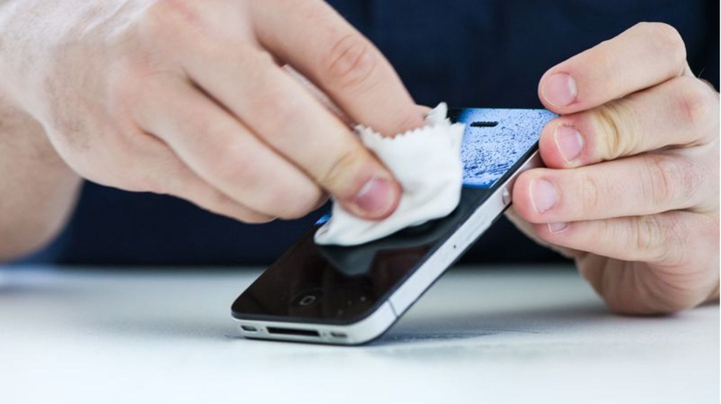 Mann wischt sein Smartphone mit einem Desinfektionstuch ab