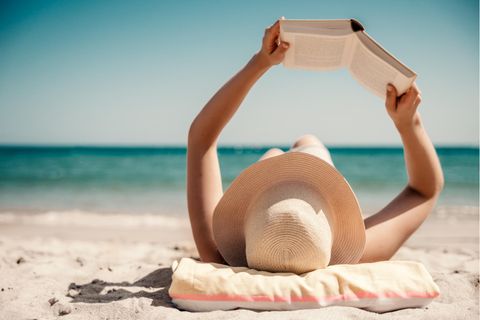Eine Person liegt am Strand und liest ein Buch