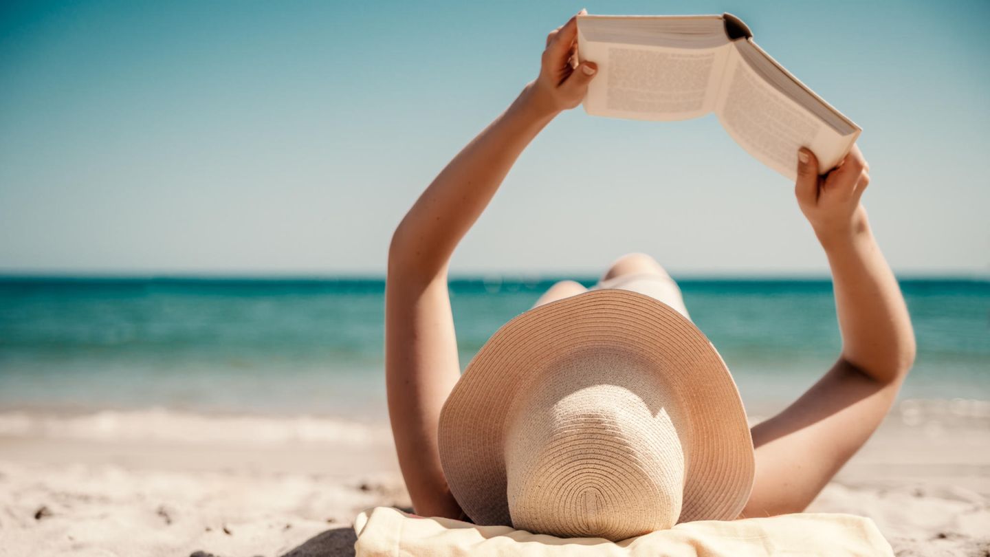Eine Person liegt am Strand und liest ein Buch