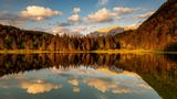 Abendlicht bei leichten Wolken am Ferchensee, oberhalb von Mittenwald. Der Waldrand und das im Hintergrund liegende Karwendel wird warm angeleuchtet und spiegelt sich im klaren Wasser des See.