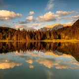 Abendlicht bei leichten Wolken am Ferchensee, oberhalb von Mittenwald. Der Waldrand und das im Hintergrund liegende Karwendel wird warm angeleuchtet und spiegelt sich im klaren Wasser des See.