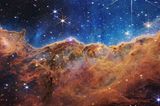 Das nahezu dreidimensionale Bild zeigt eine Region im riesigen Carina-Nebel, die Astronomen und Astronominnen die „kosmischen Kliffs“ nennen. In dem blauen Hintergrund schweben tausende junge, sehr massereiche Sterne. Die starke UV-Strahlung und die Sonnenwinde, die von ihnen ausgehen, formen im Rand der braunen Gas- und Staubwolke bizarre Strukturen, die zum Teil mehrere Lichtjahre groß sind. Dank der „Infrarot-Augen“ des neuen Teleskops kommen so bislang ungesehene Strukturen zutage