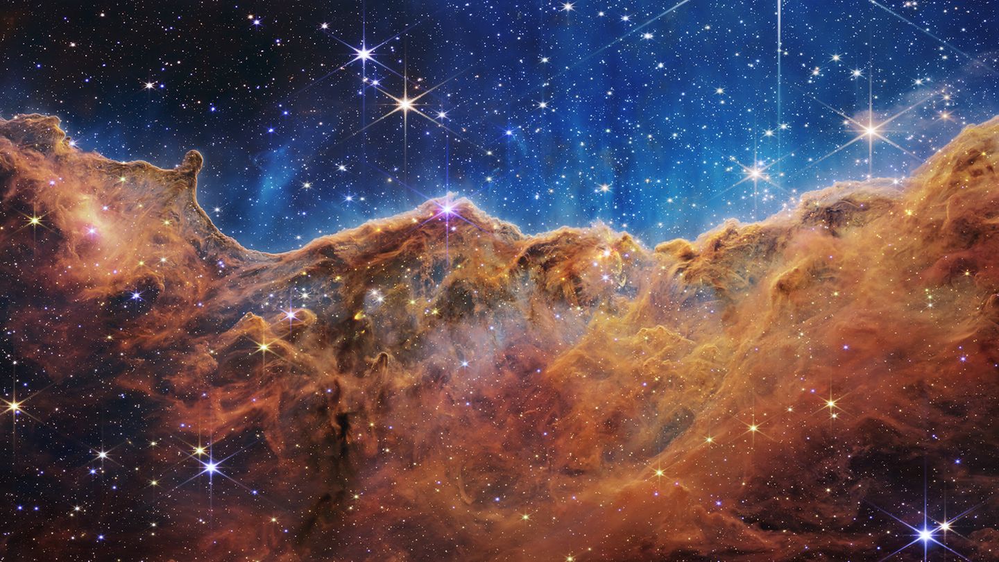 Carina-Nebel Das nahezu dreidimensionale Bild zeigt eine Region im riesigen Carina-Nebel, die Astronomen und Astronominnen die „kosmischen Kliffs“ nennen. In dem blauen Hintergrund schweben tausende junge, sehr massereiche Sterne. Die starke UV-Strahlung und die Sonnenwinde, die von ihnen ausgehen, formen im Rand der braunen Gas- und Staubwolke bizarre Strukturen, die zum Teil mehrere Lichtjahre groß sind. Dank der „Infrarot-Augen“ des neuen Teleskops kommen so bislang ungesehene Strukturen zutage
