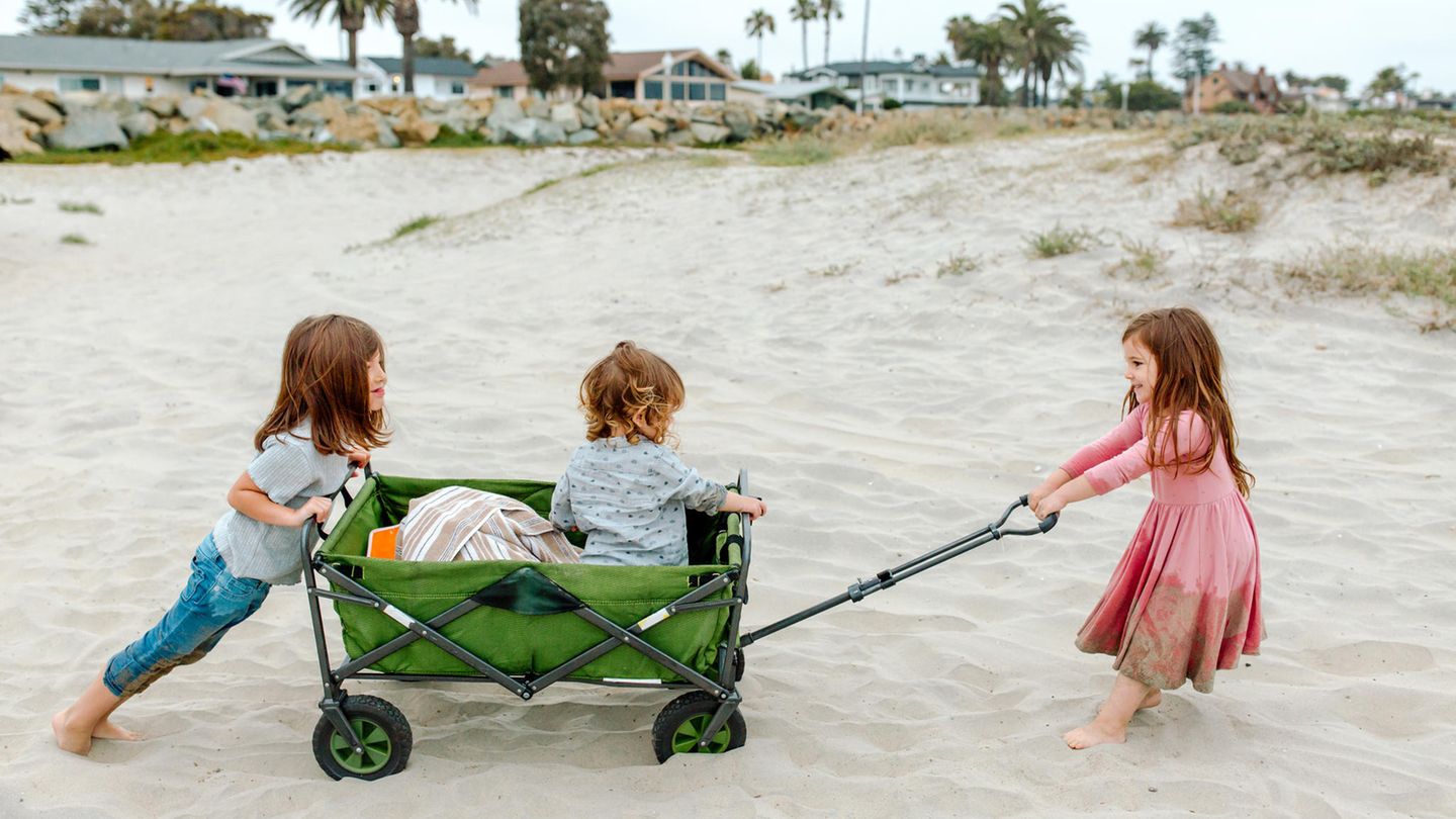Drei Kinder mit einem faltbaren Bollerwagen am Strand.