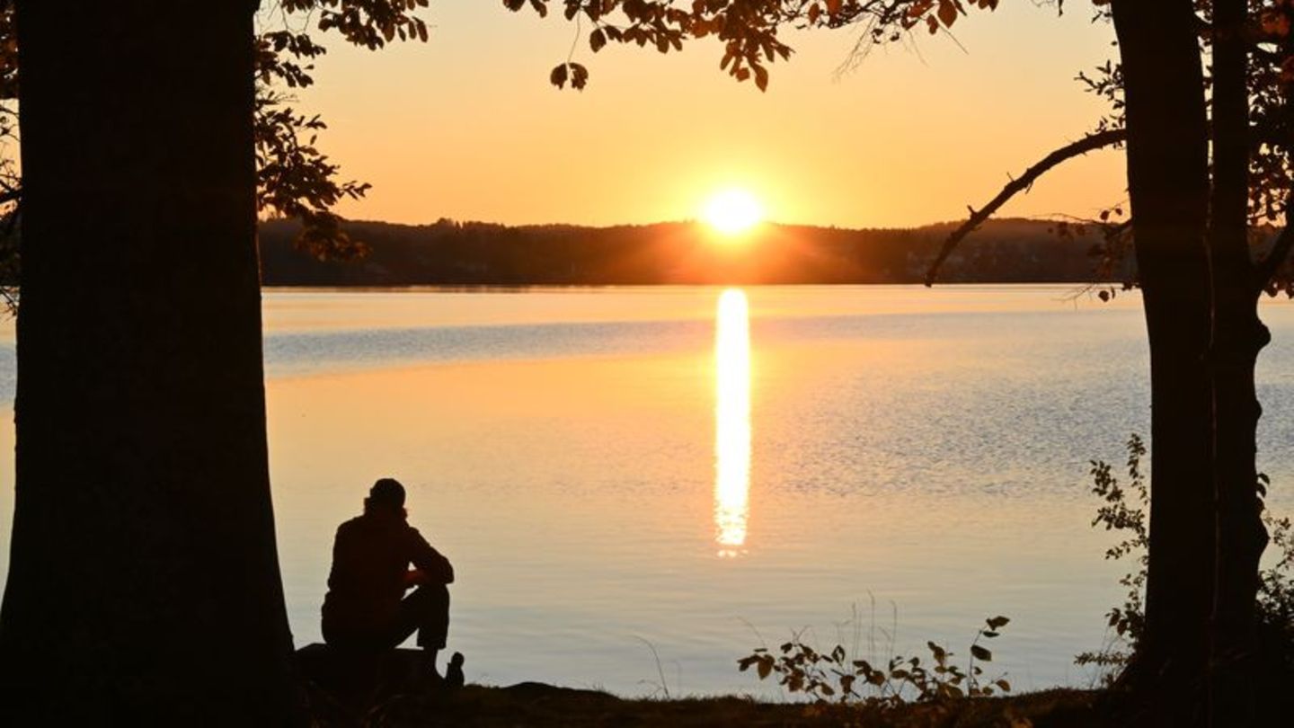 Eine Person sitzt bei Sonnenuntergang an einem See