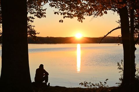 Eine Person sitzt bei Sonnenuntergang an einem See