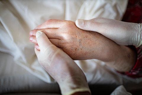 Pfleger mit Handschuhen hält die Hand eines alten Menschen