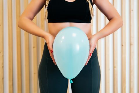 Frau hält einen Luftballon vor ihren Bauch und Schambereich