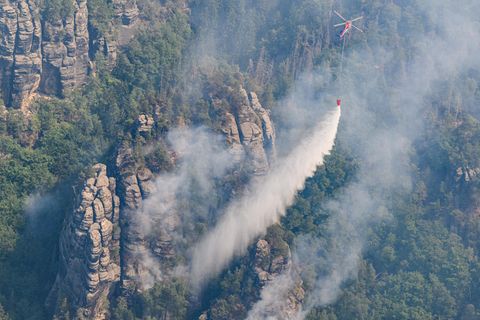 Ein Lastenhubschrauber aus Österreich fliegt mit einem Löschwasser-Außenlastbehälter um einen Waldbrand im Nationalpark Sächsische Schweiz zu löschen. 28.07.