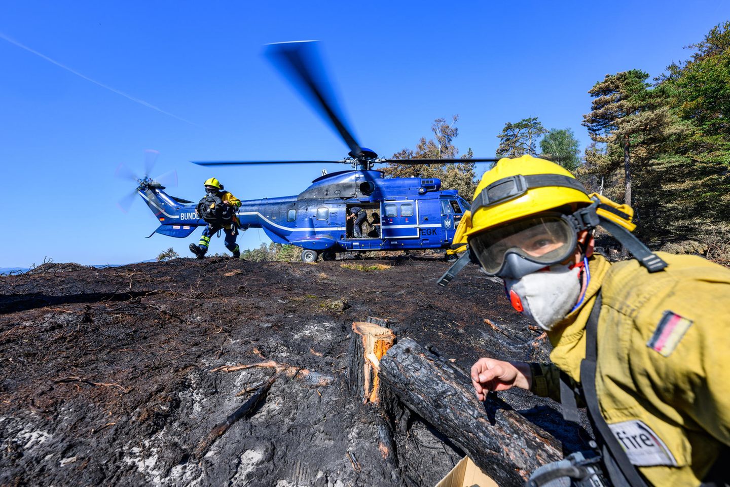 Sie werden von freiwilligen Feuerwehrleuten des Internationalen Katastrophenschutzes Deutschland unterstützt, die am Boden nach verbleibenden Glutnester suchen und diese löschen