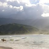 Ein Surfer geht mit seinem Brett ins Wasser. Im Hintergrund sind Berge