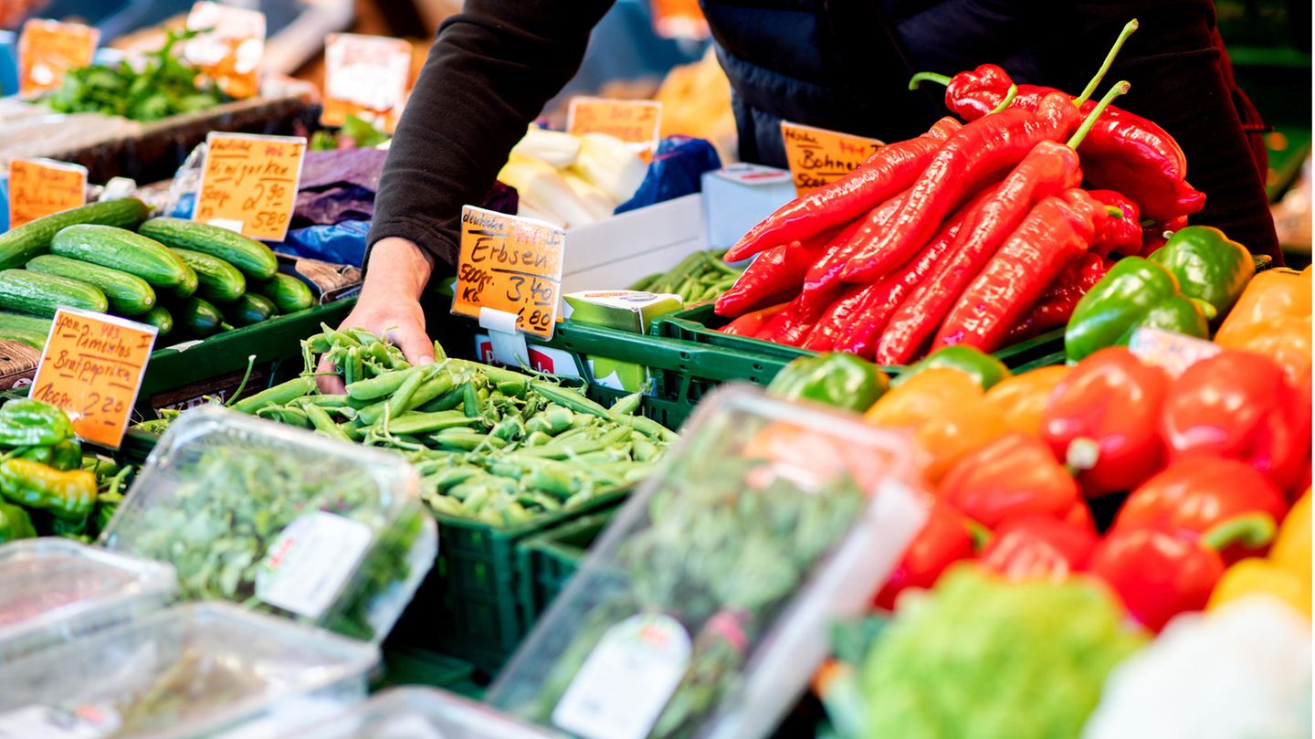 Ein Verkäufer greift an einem Obst- und Gemüsestand auf dem Wochenmarkt in eine Kiste mit Erbsen Ein Verkäufer greift an einem Obst- und Gemüsestand auf dem Wochenmarkt in eine Kiste mit Erbsen