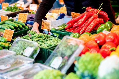 Ein Verkäufer greift an einem Obst- und Gemüsestand auf dem Wochenmarkt in eine Kiste mit Erbsen