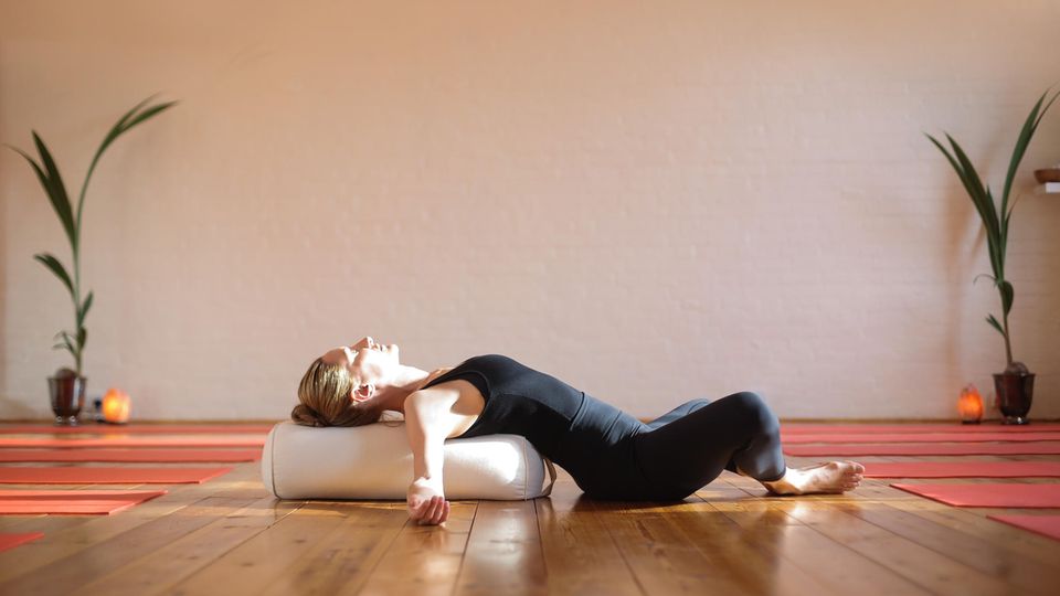 Eine Frau nutzt ein Yoga Bolster als Yoga Zubehör und nutzt es als Unterstützen in der liegenden Rückbeuge. Eine Frau nutzt ein Yoga Bolster als Yoga Zubehör und nutzt es als Unterstützen in der liegenden Rückbeuge.
