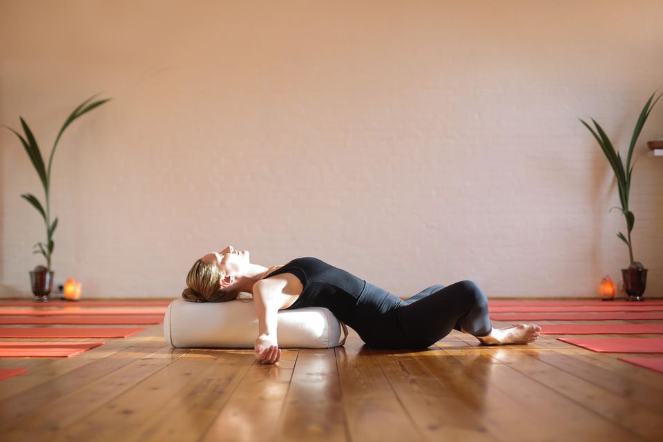 Eine Frau nutzt ein Yoga Bolster als Yoga Zubehör und nutzt es als Unterstützen in der liegenden Rückbeuge.