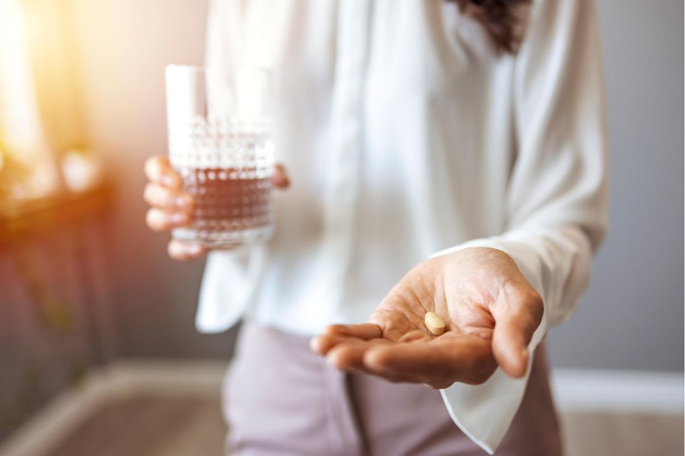 Eine Frau hält in der einen Hand eine Tablette, in der anderen ein Wasserglas