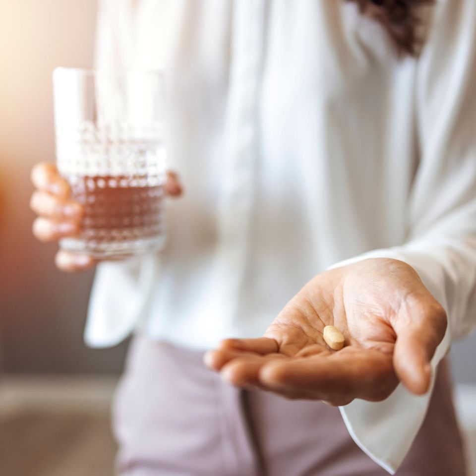 Eine Frau hält in der einen Hand eine Tablette, in der anderen ein Wasserglas