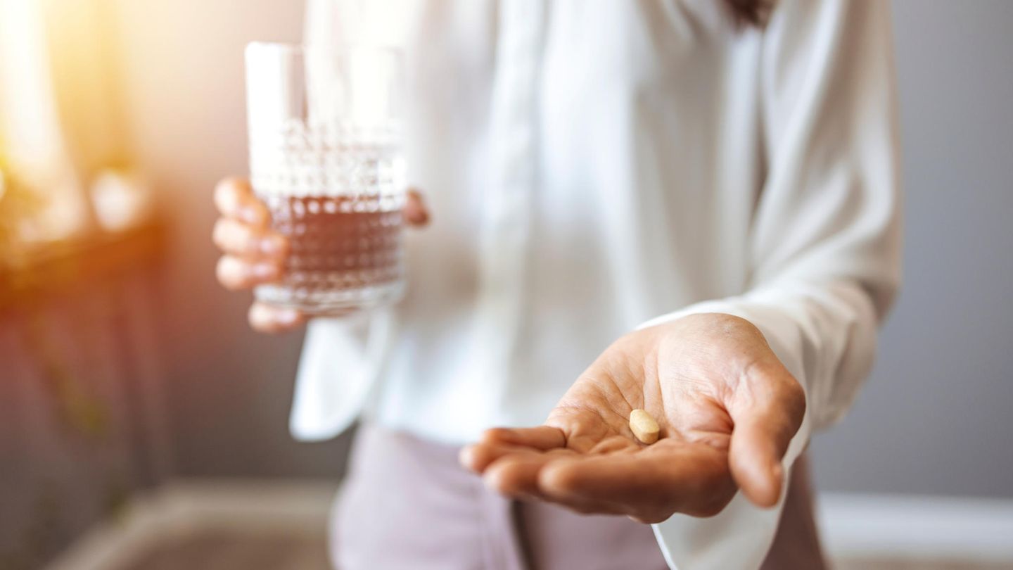 Eine Frau hält in der einen Hand eine Tablette, in der anderen ein Wasserglas