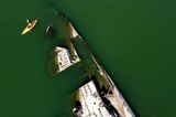 Ein Kajakfahrer paddelt auf der Donau an einem Wrack eines Kriegsschiffs aus dem Zweiten Weltkrieg