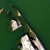 Ein Kajakfahrer paddelt auf der Donau an einem Wrack eines Kriegsschiffs aus dem Zweiten Weltkrieg