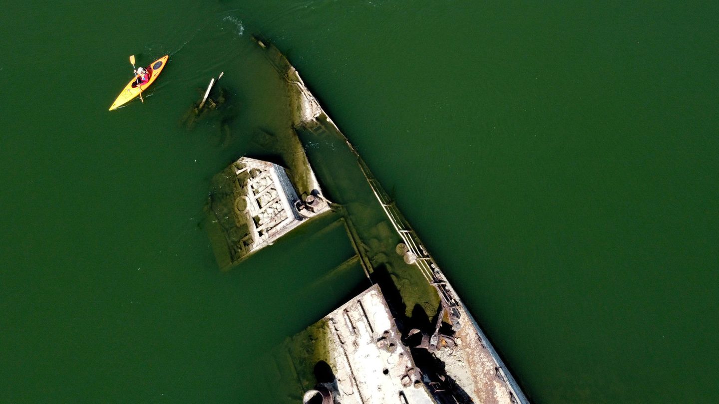 Ein Kajakfahrer paddelt auf der Donau an einem Wrack eines Kriegsschiffs aus dem Zweiten Weltkrieg