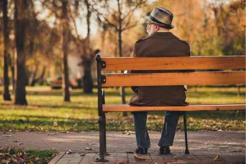 Alter Mann mit Hut und Stock sitzt auf einer Bank