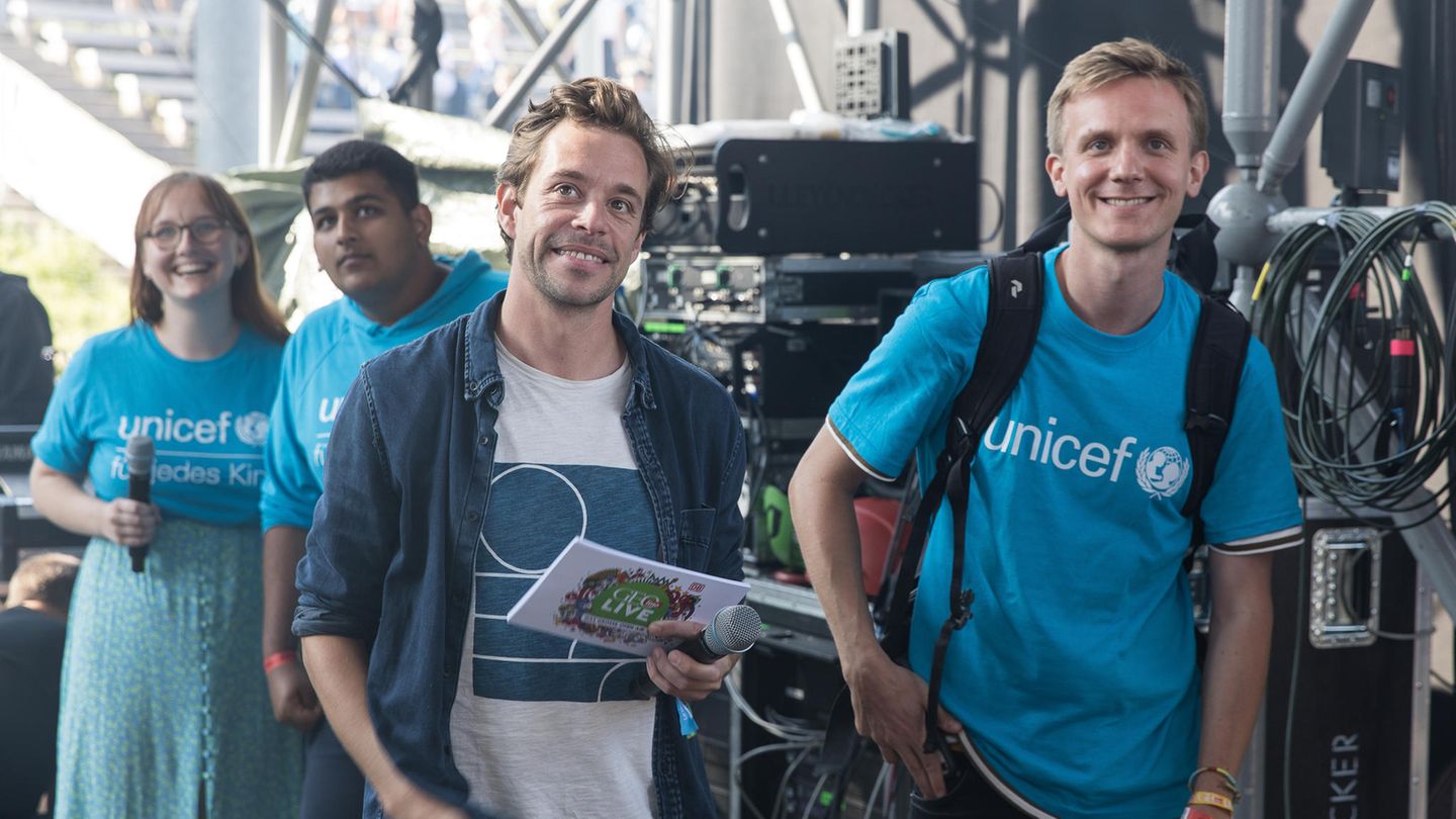 Tobias Krell alias "Cecker Tobi" (2. von rechts) steht mit Moderationskarten und einem Mikrofon hinter der Bühne.