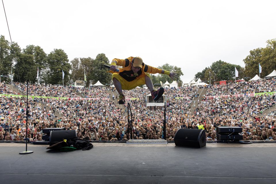 Der Künstler DONIKKL springt auf der Bühne hoch in die Luft, im Hintergrund sieht man ganz viele Menschen im Publikum.