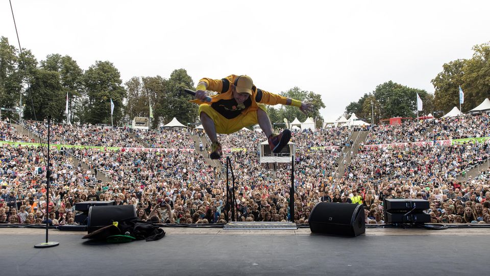 Der Künstler DONIKKL springt auf der Bühne hoch in die Luft, im Hintergrund sieht man ganz viele Menschen im Publikum.