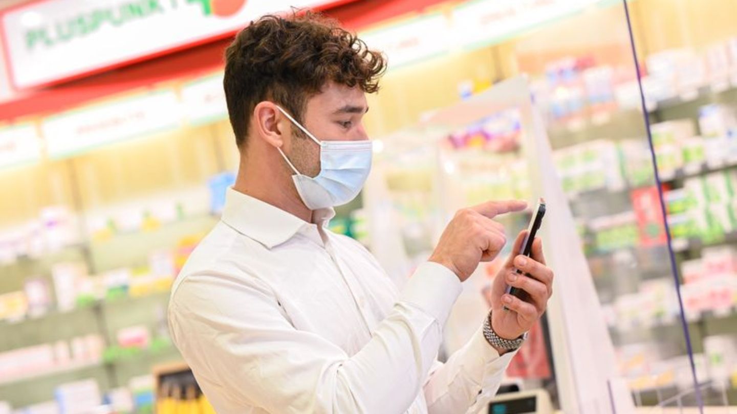 Junger Mann mit Smartphone vor einer Apotheke