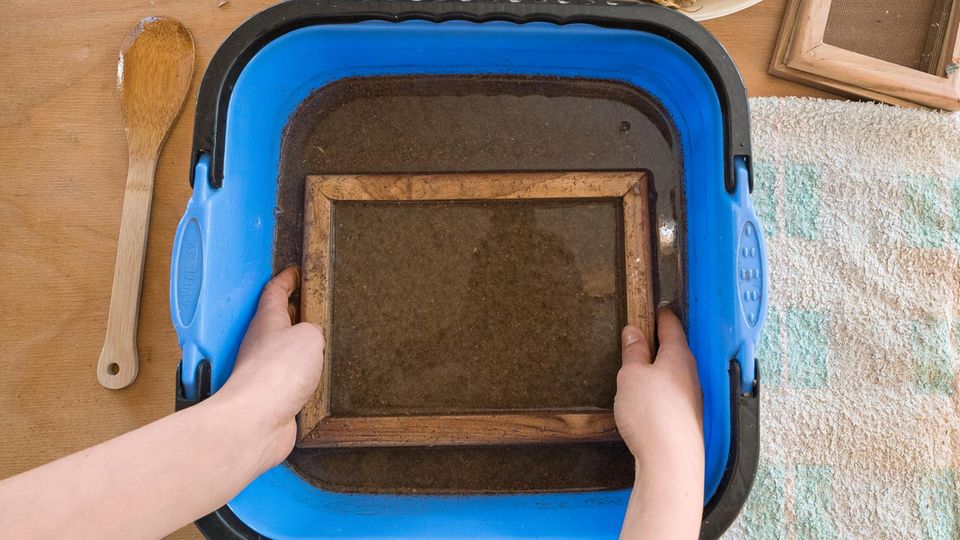 In eine quadratische Wanne mit brauner Flüssigkeit wird ein Schöpfrahmen eingetaucht.