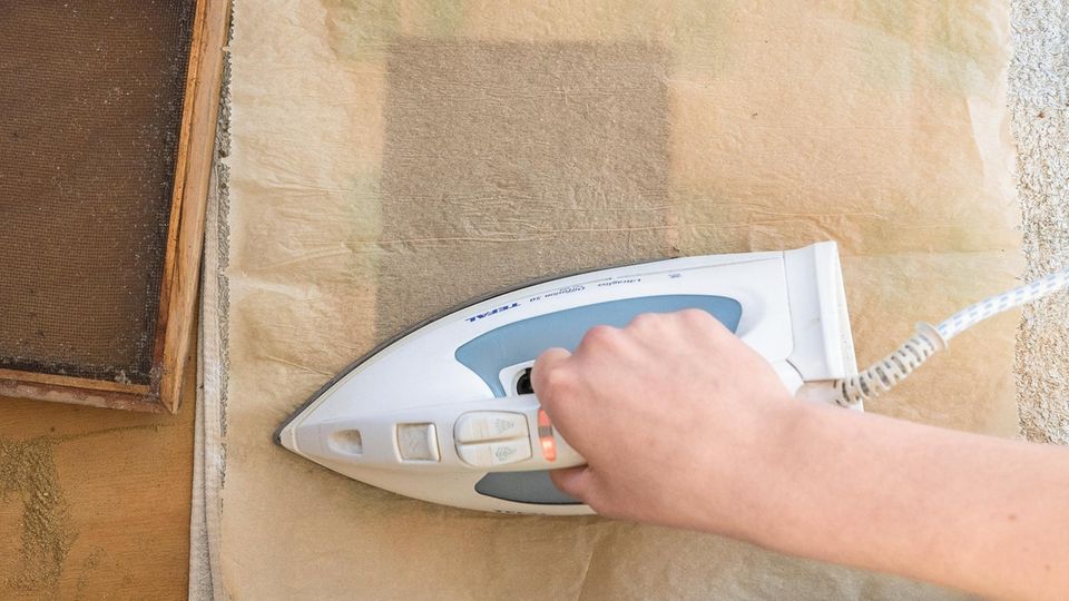 Mit einem Bügeleisen wird das Papier gebügelt, das von Backpapier bedeckt ist.