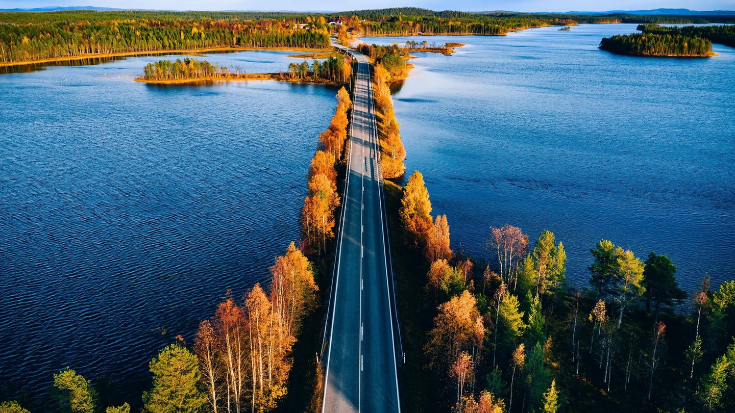 Luftaufnahme einer Brücke über blaues Gewässer in einem bunten Herbstwald in Finnland