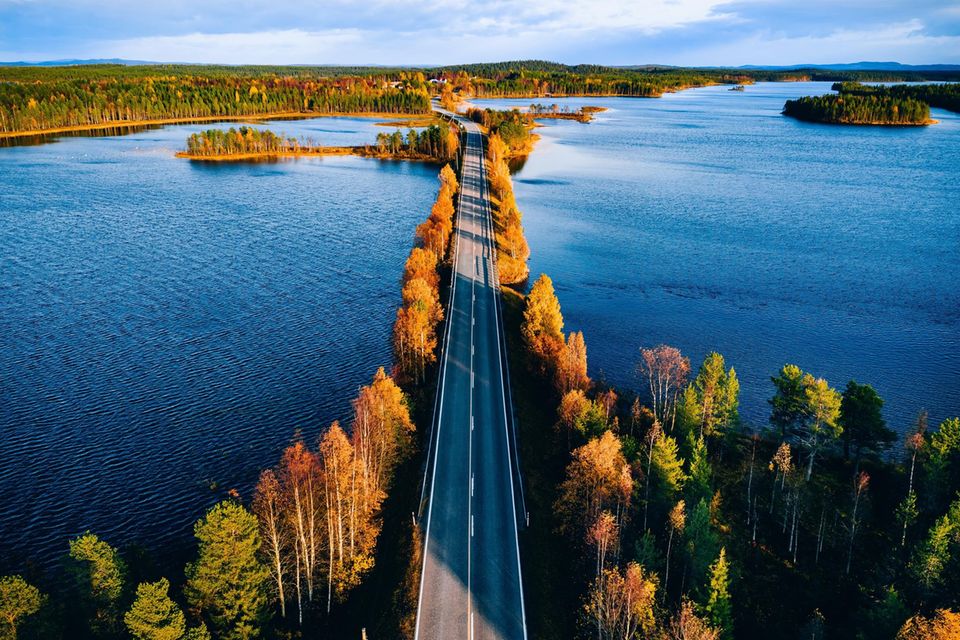 Luftaufnahme einer Brücke über blaues Gewässer in einem bunten Herbstwald in Finnland