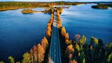 Luftaufnahme einer Brücke über blaues Gewässer in einem bunten Herbstwald in Finnland