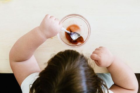 Von oben fotografiert: Kind mit dickeren Armen löffelt einen Dessert