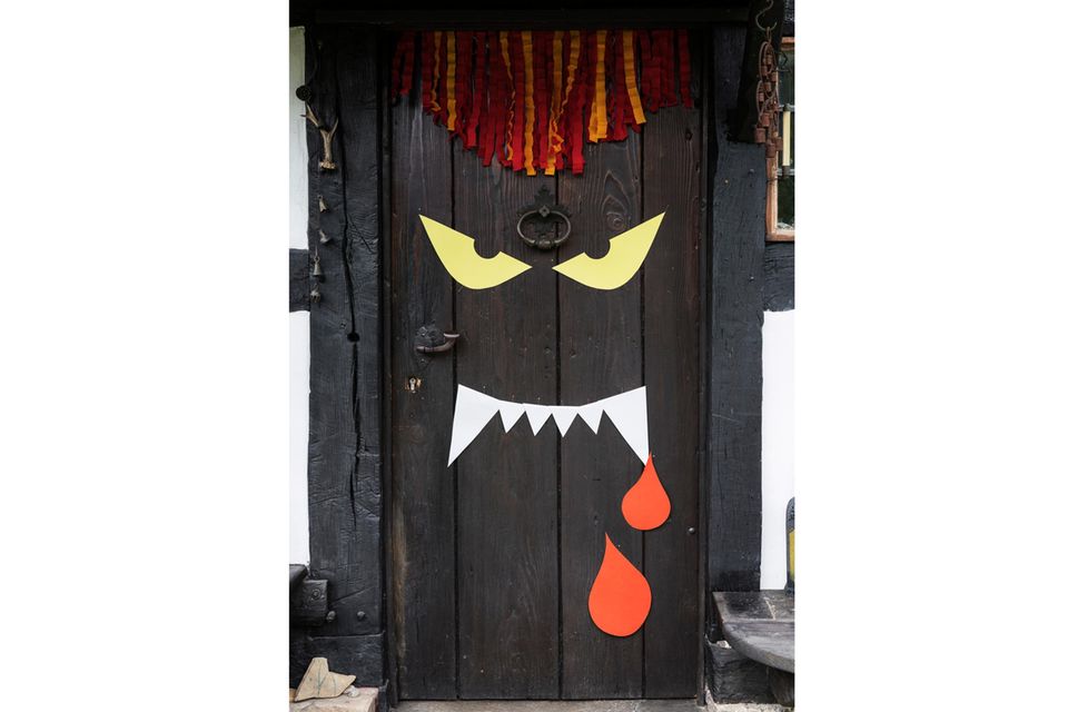 Eine braune Tür, darauf sind gelbe Monster-Augen, spitze Zähne und rote Tropfen aus Papier zu sehen.
