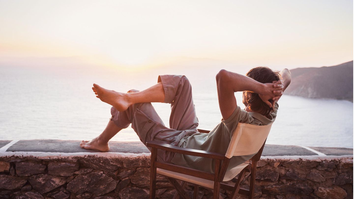 Mann sitzt im Stuhl und bewundert den Sonnenuntergang am Meer