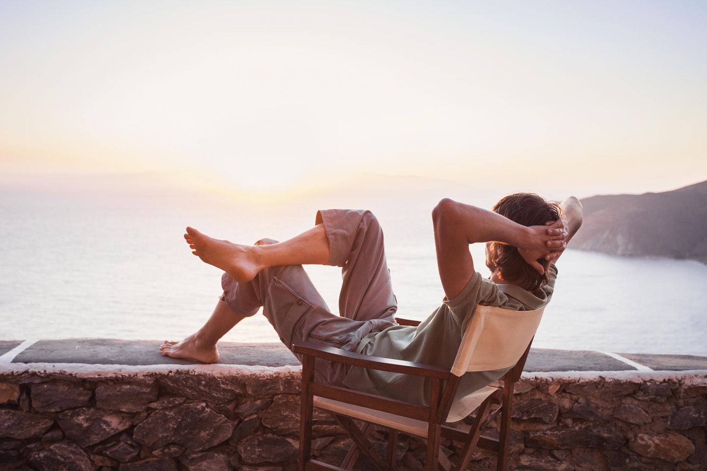 Mann sitzt im Stuhl und bewundert den Sonnenuntergang am Meer