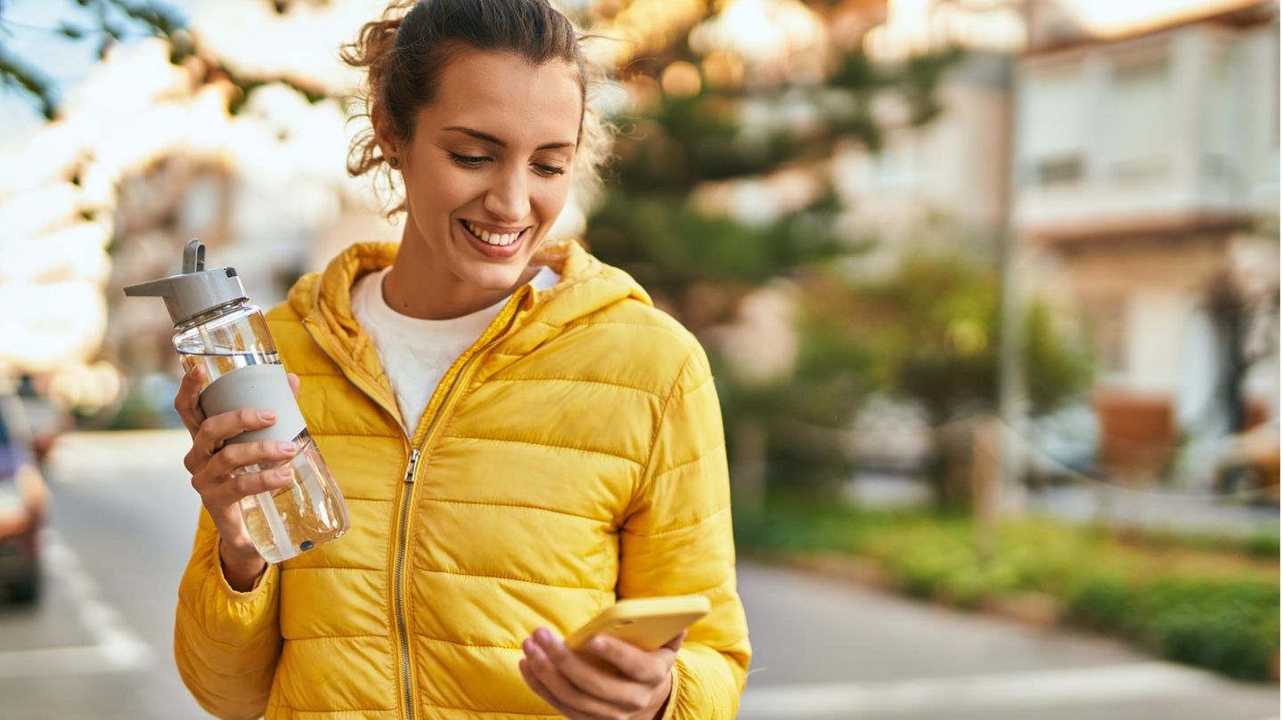 eine Frau mit einer Wasserflasche und Handy in der Hand