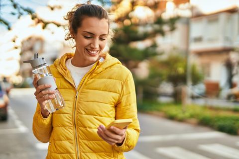eine Frau mit einer Wasserflasche und Handy in der Hand