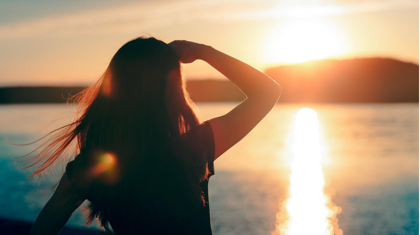 Junge Frau schaut über das Wasser in den Sonnenuntergang / Gesetz der Anziehung