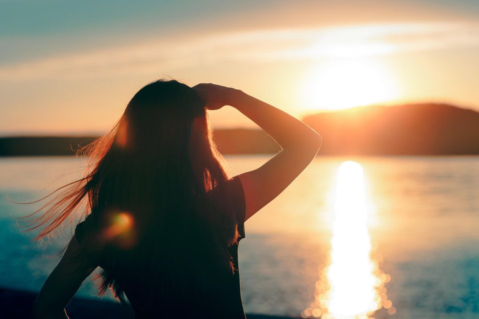 Junge Frau schaut über das Wasser in den Sonnenuntergang / Gesetz der Anziehung