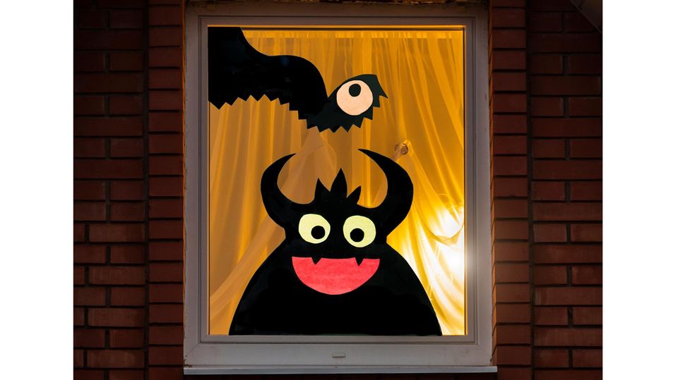 Ein Fenster von außen mit einem weißen Vorhang, von drinnen scheint ein Licht. Auf dem Fenster sind zwei Monster zu sehen.