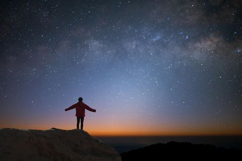 Eine Person steht auf einer Anhöhe und streckt seine Arme aus. Im Hintergrund sieht man den Nachthimmel.